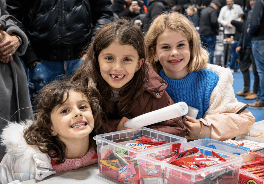 Three young girls with excited expressions are looking at the camera over clear plastic boxes filled with sweets, ready to make this Bonfire Night an evening to remember.